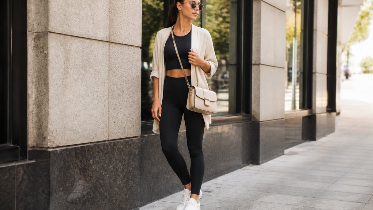 A person styles lifestyle activewear with a beige cardigan and leather trainers in an urban setting.