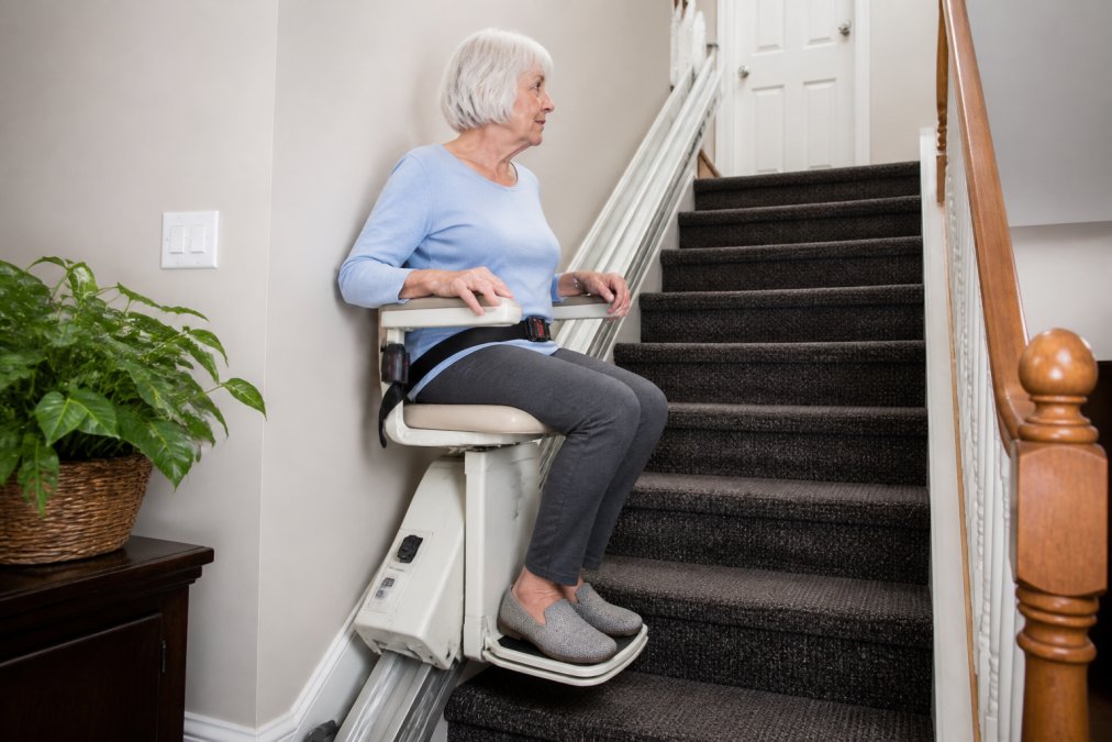 Older adult using a stairlift to safely navigate residential stairs in a home setting, showing proper seating and handrail positioning