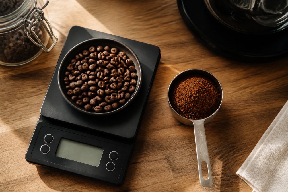 Kitchen scale with coffee beans and a scoop of grounds to measure roast caffeine on a wooden countertop