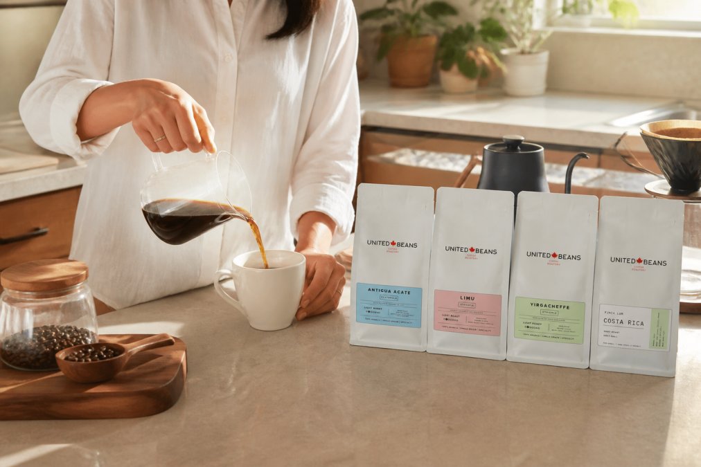 Person pouring freshly brewed light roast coffee into a white cup with whole bean bags and brewing equipment arranged on a kitchen counter in natural morning light