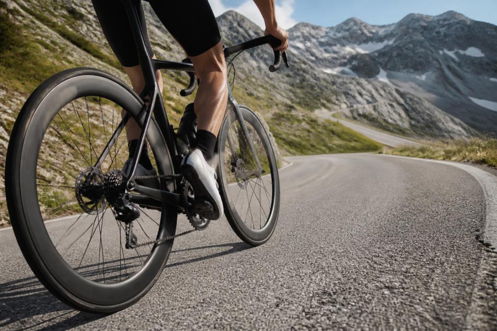 A cyclist riding a road bike up a steep mountain pass, with a close-up focus on the carbon wheelset and its deep rims in motion