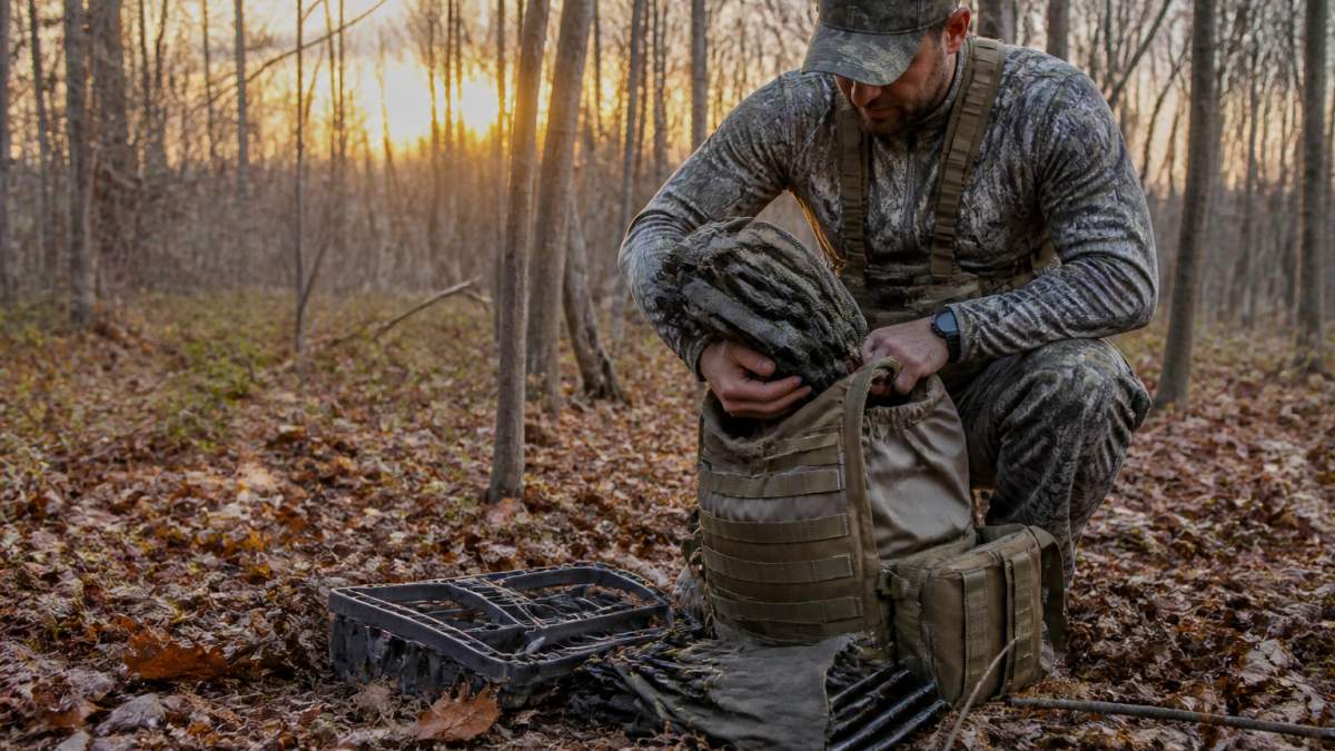 Hunter organizing climbing sticks and a hunting saddle into a minimalist pack on the forest floor at dawn