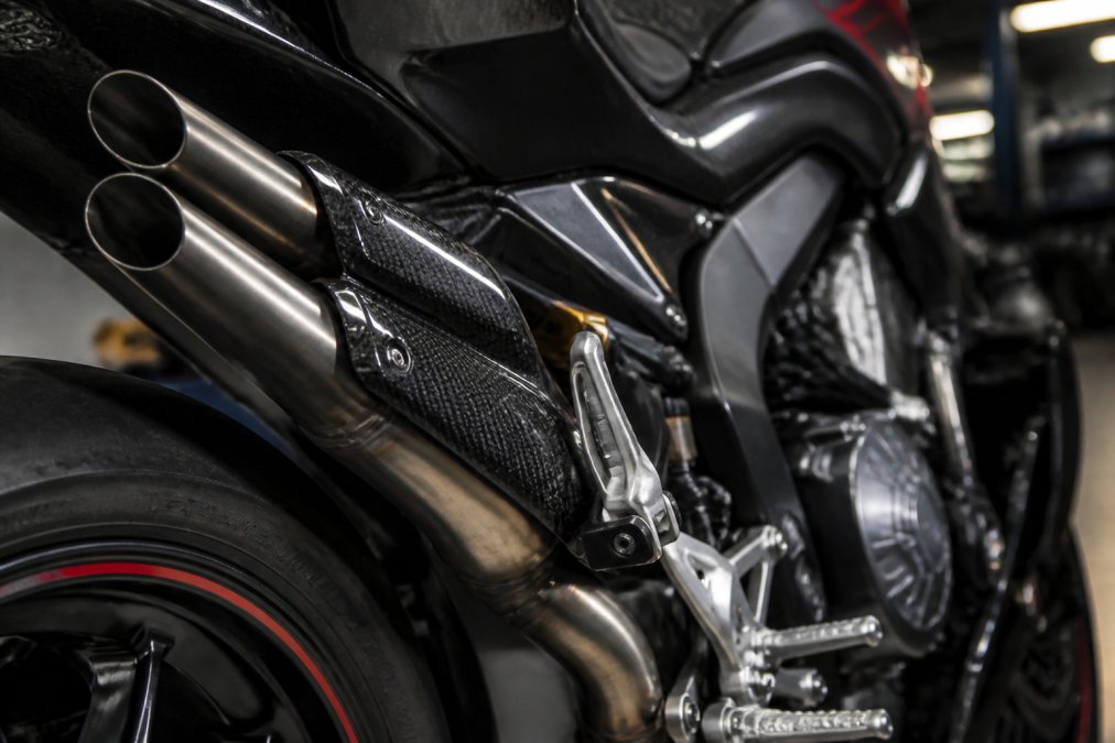 Close-up van titanium uitlaatonderdelen en carbon-elementen op een limited edition motorfiets, met professionele werkplaatsverlichting die de premium afwerking benadrukt