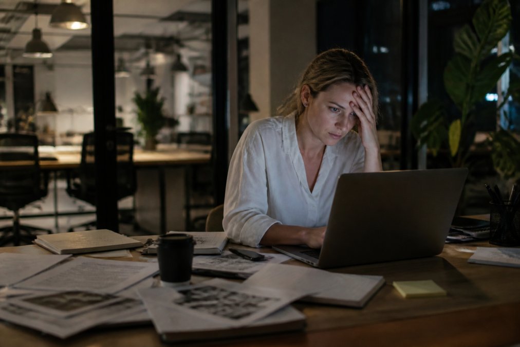 A founder working alone at a desk late at night, surrounded by papers and a laptop, looking overwhelmed while their team has already left the office