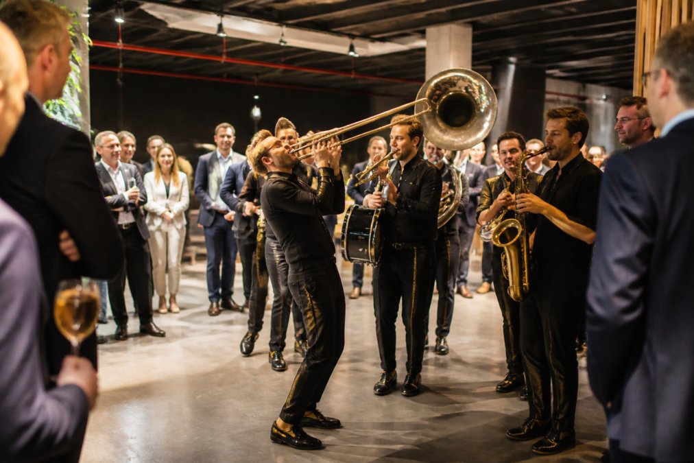 Energieke brassband verzorgt live muziek tijdens een productpresentatie in een moderne bedrijfsruimte voor zakelijk publiek.