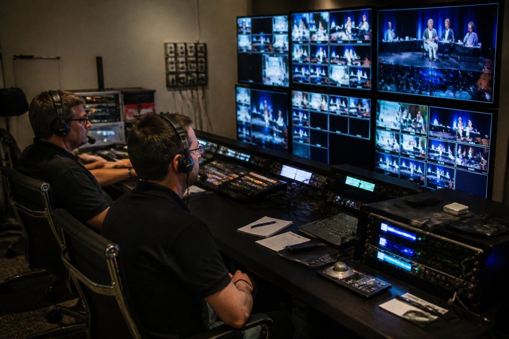 Professional broadcast control room with multiple monitors displaying live event feeds, technicians in headsets monitoring real-time streaming data and analytics on darkened screens