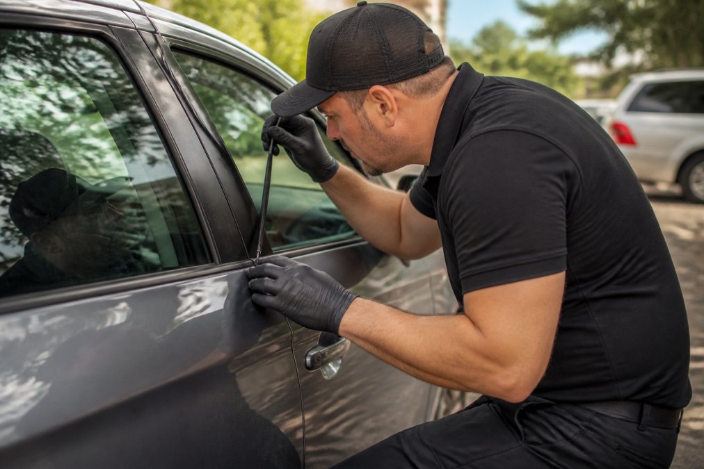 Mobile locksmith technician using specialized equipment to open a car door, demonstrating professional automotive lockout assistance in daylight