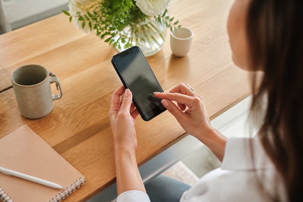 Gros plan des mains d'un coach utilisant un smartphone pour consulter son calendrier de séances, avec un écran affichant des fonctionnalités de planification et de rappels automatisés