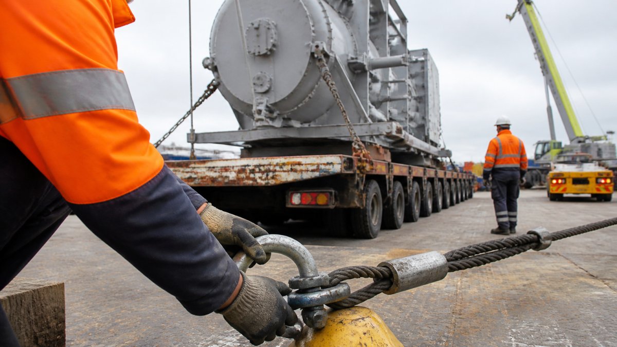 Heavy haulage crew loading an oversized cargo unit onto a low-loader trailer at a freight yard