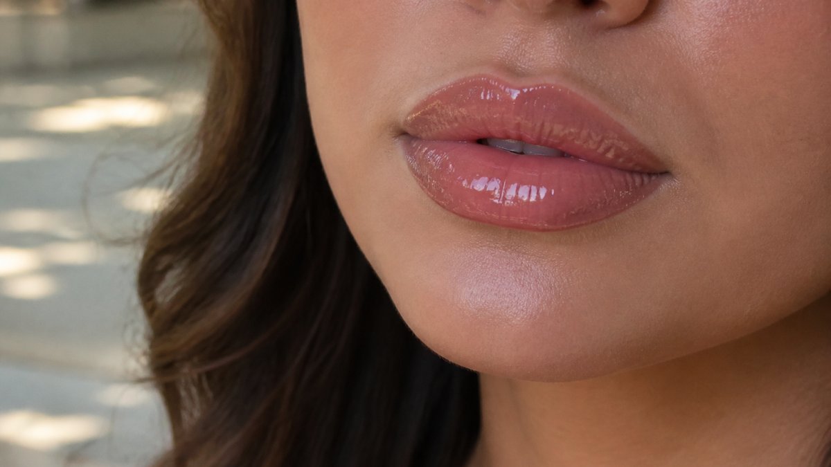 Close-up of a woman's lips wearing high-shine gloss in natural daylight, showing mirror-bright finish and depth of color payoff with soft focus background
