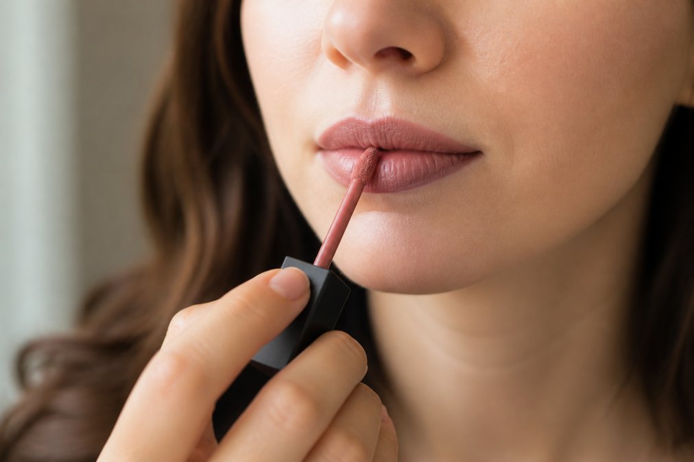 Close-up of hands applying long-lasting matte liquid lipstick with a precision applicator to clean, prepped lips, showing proper angle and technique with natural lighting