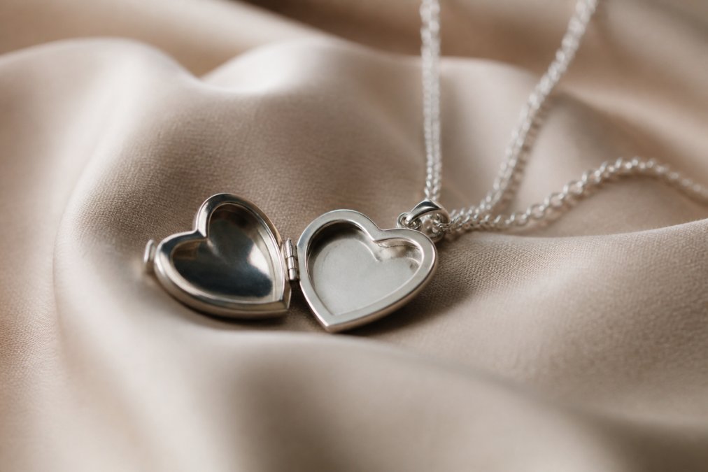 Close-up of an elegant hidden message engraved necklace displayed on soft fabric with warm lighting highlighting the metallic details and the interior engraving visible inside the pendant