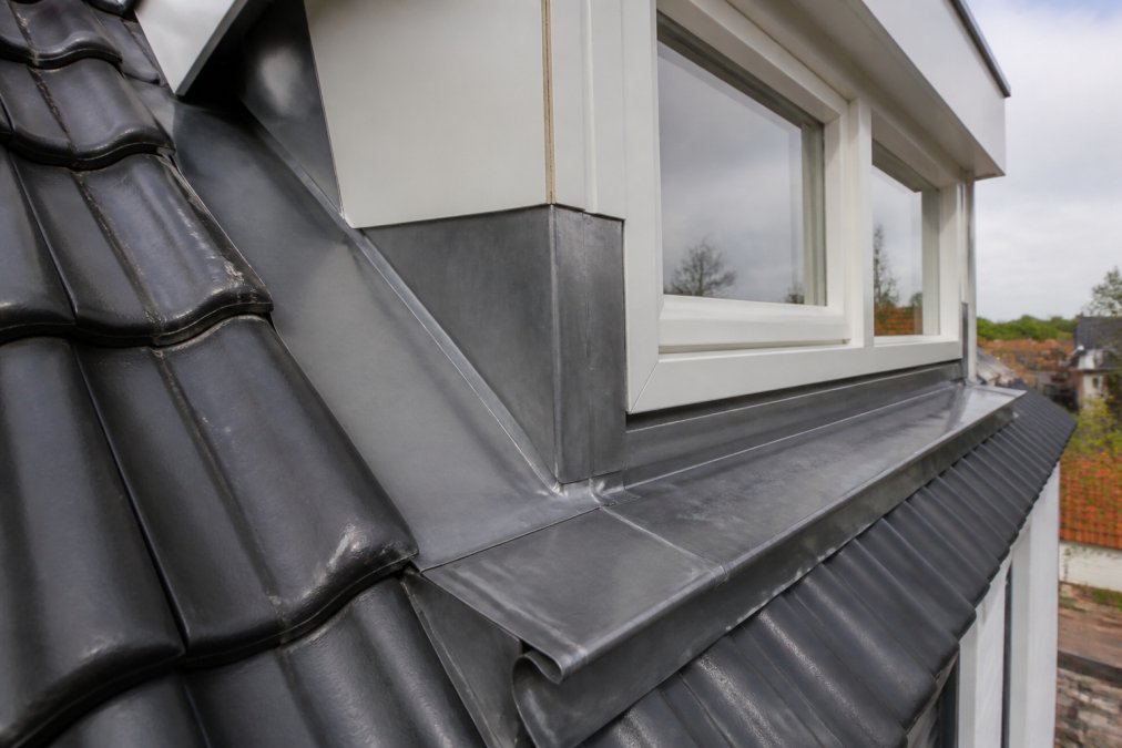 Close-up van vakkundig gevormde loodafsluiting bij dakkapel, met zichtbare verholen goot en nette aansluitingen op metselwerk