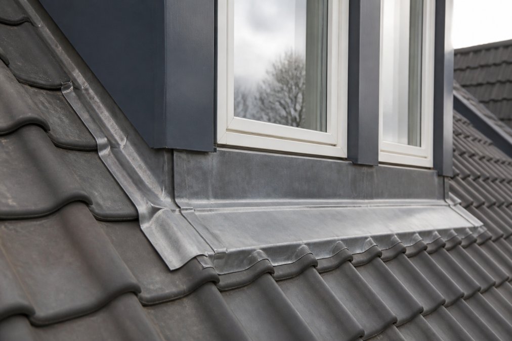 Close-up van een waterdichte loodaansluiting rond een dakkapel met duidelijk zichtbare overlappingen en professionele afwerking op een hellend dak