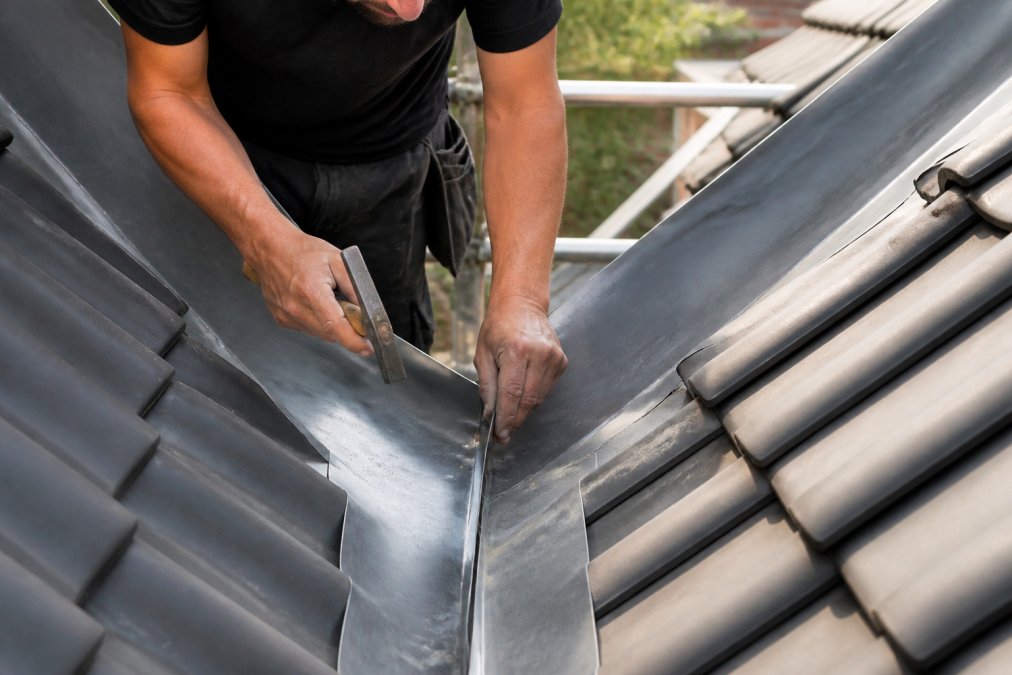 Loodklopper die voorzichtig bladlood vormgeeft en aanpast in een dakvalleigoot met gereedschap, werkt nauwkeurig met handen en professionele instrumenten in daglicht