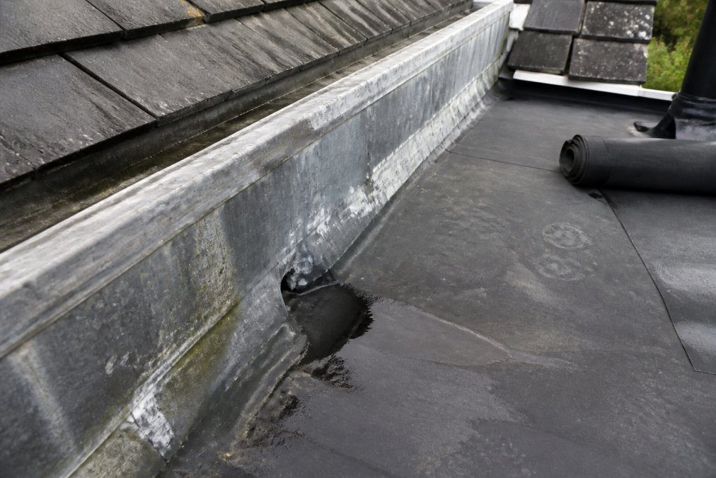 Close-up inspectie van kilgoot met zichtbare slijtage, scheuren en watervlekken op het dak, voorbereiding voor dakrenovatie