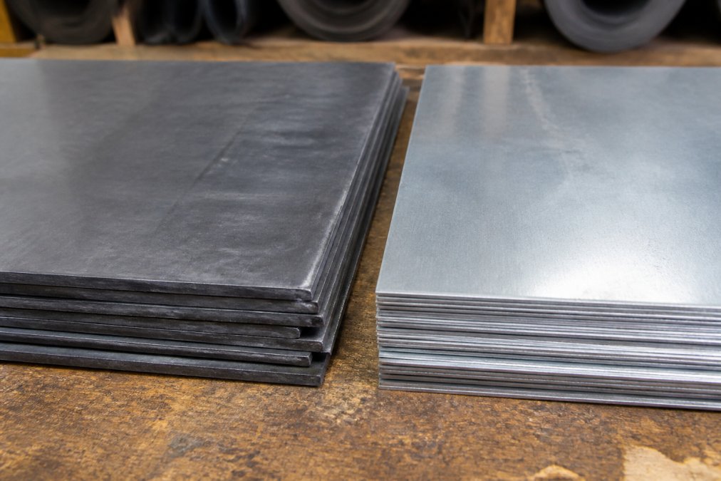 Close-up van loodslabben en zinken platen naast elkaar op een werkblad, met duidelijke kleurcontrasten tussen donkergrijs lood en zilvergrijs zink