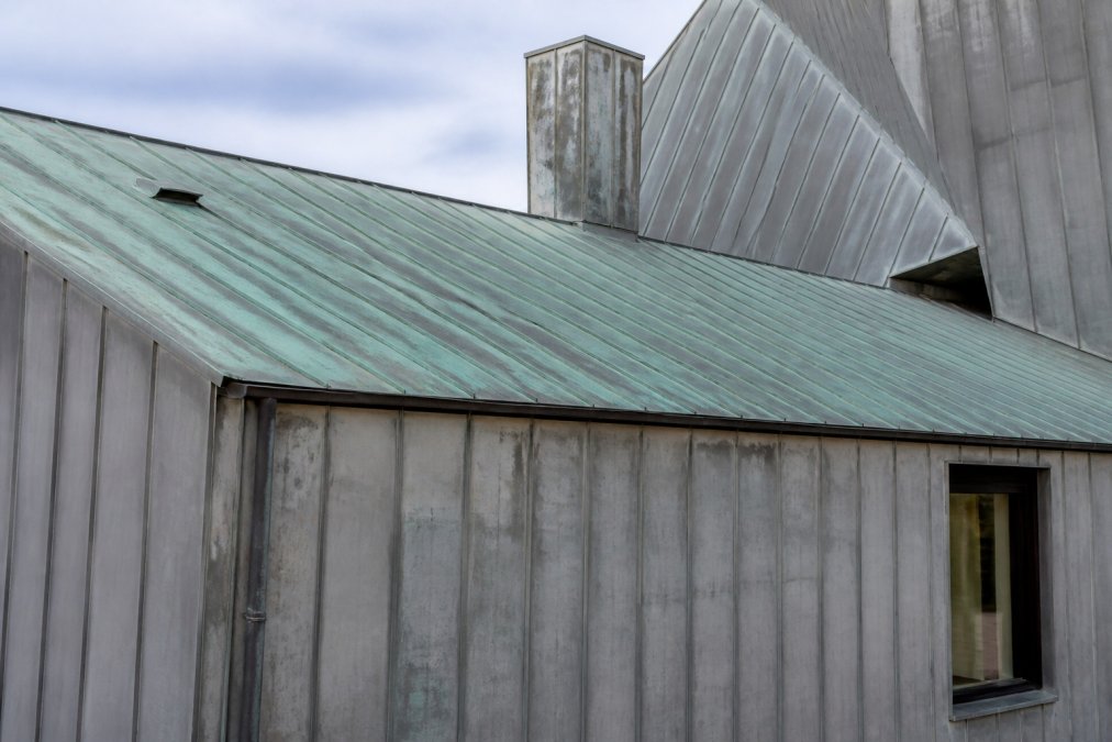 Gevelbekleding met zichtbare patina-vorming op zinkwerk, toont groene en grijze oxidatielaag op dak en gevel na jaren blootstelling aan weer