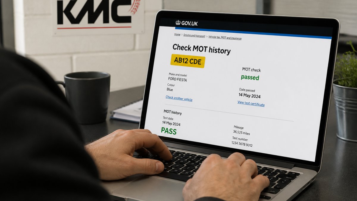 Close-up of hands using a laptop to access the DVSA MOT history checker, showing vehicle registration details and MOT status on the screen with natural office lighting