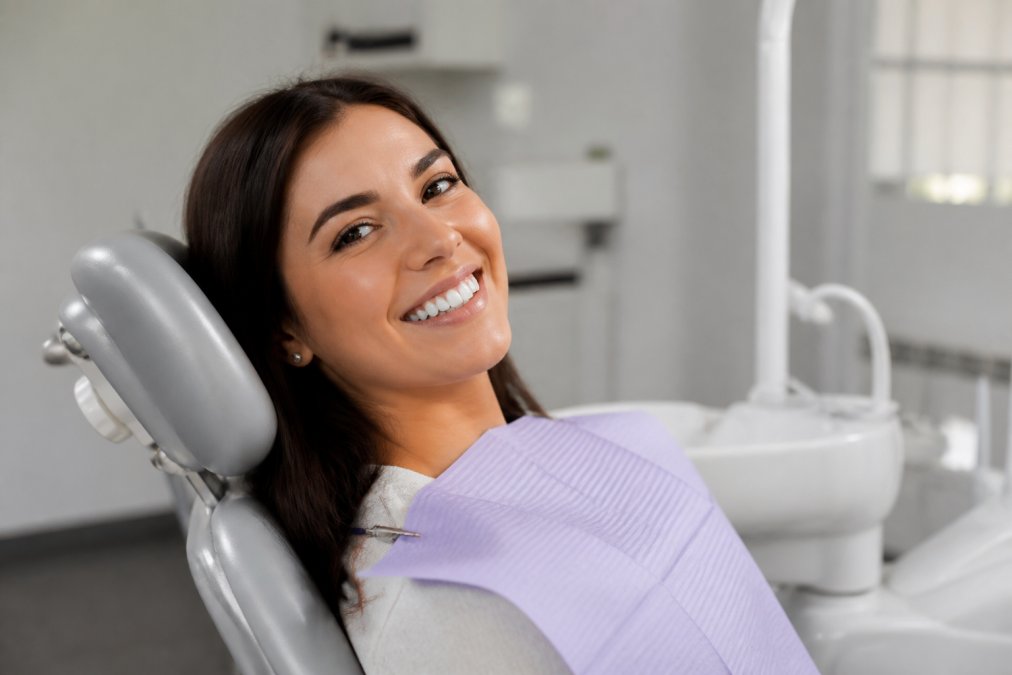 Patient smiling in a modern dental chair with natural lighting, showing healthy restored teeth and comfortable treatment environment