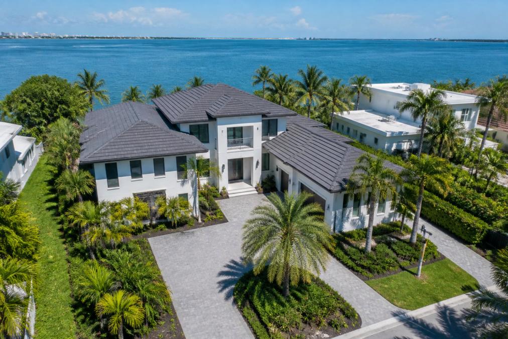 Aerial view of a luxury waterfront home in Florida with modern architecture, surrounded by mature landscaping and ocean or bay visible in the background