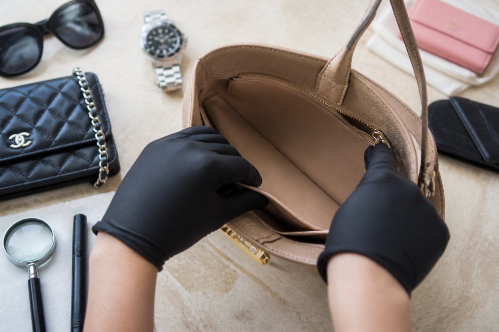 Hands carefully examining interior of luxury designer handbag, checking lining condition and authenticity markers under bright, natural lighting