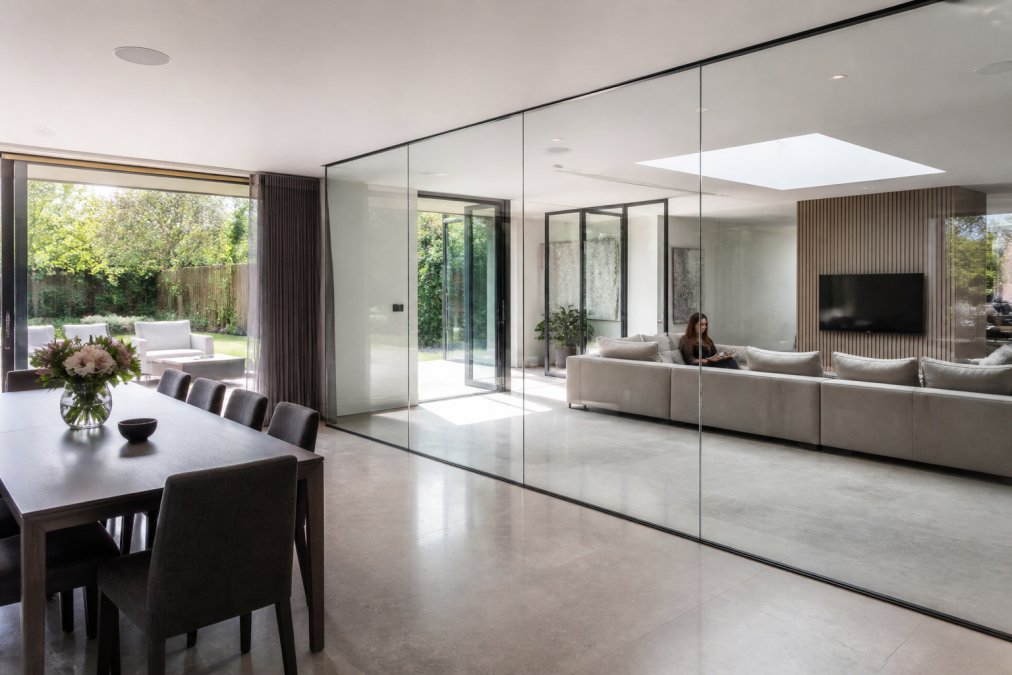 Bright open-plan living room featuring elegant glass design with floor-to-ceiling partitions separating the lounge.