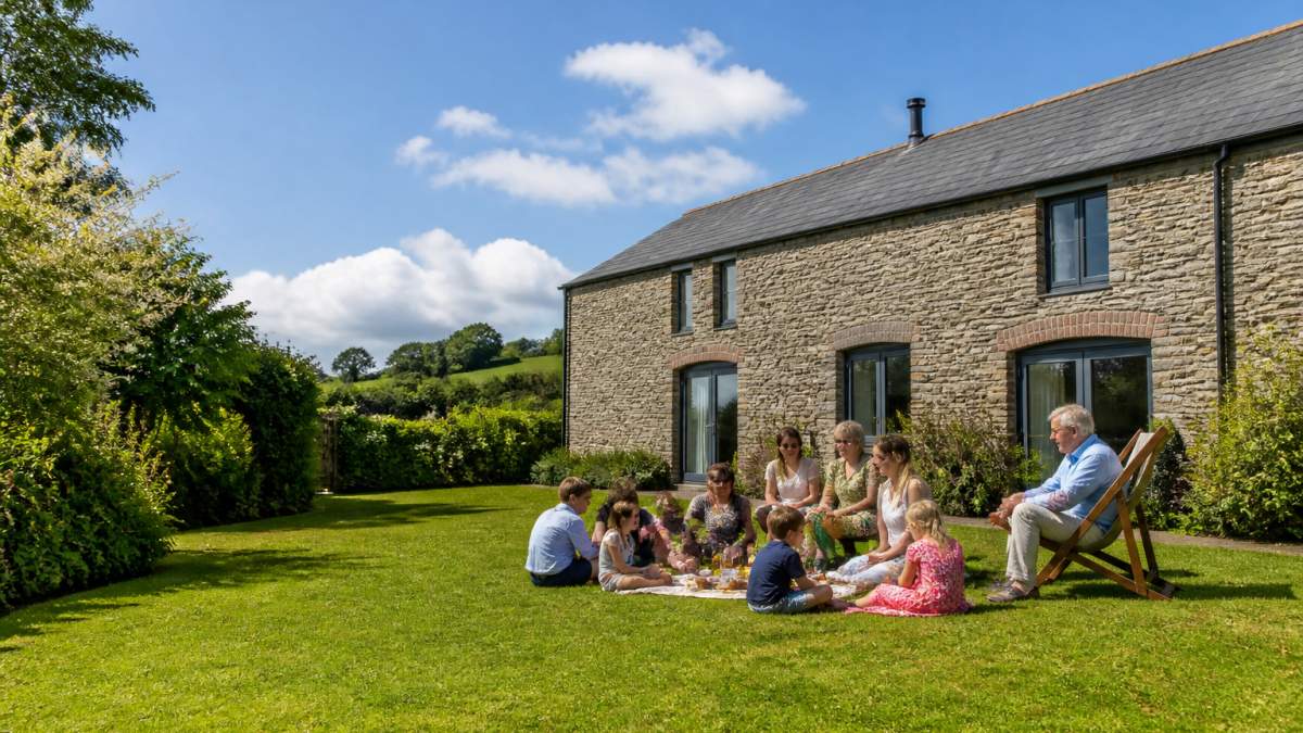 A spacious converted stone barn with a fully enclosed garden, countryside views, and a family group relaxing outside on a sunny day in Devon