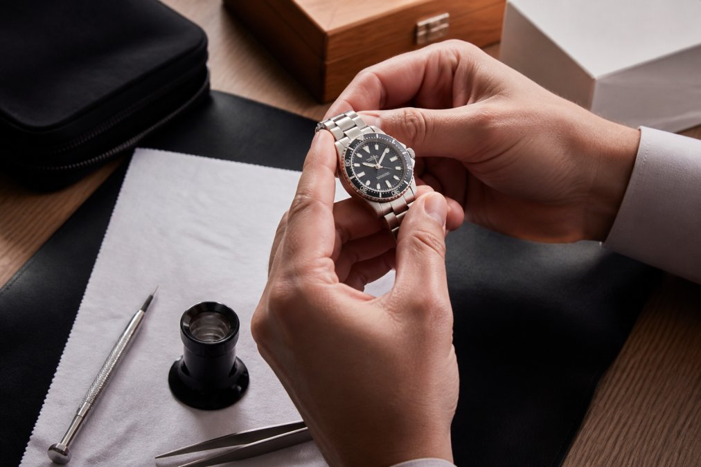 Hands carefully examining a luxury watch under natural light, checking the dial details and case with a jeweler's loupe nearby on a soft white cloth