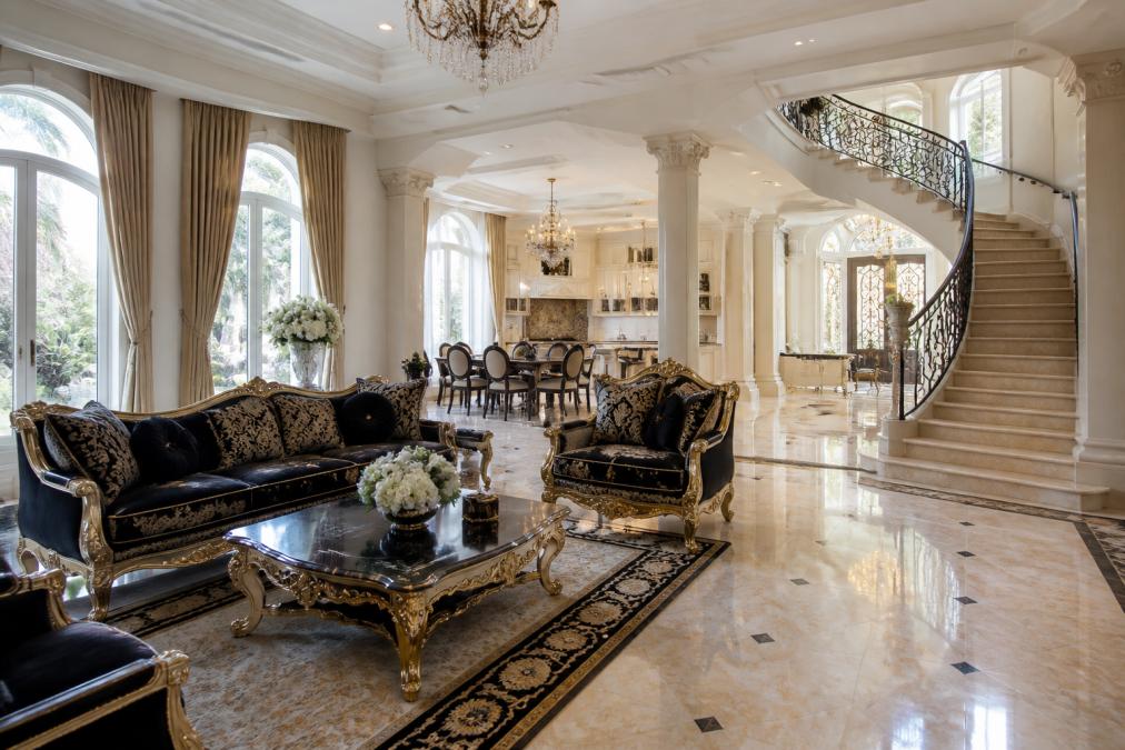 Großzügiger offener Wohnbereich mit barocken Designermöbeln, harmonischer Raumaufteilung mit verschiedenen Funktionszonen, natürliches Lichteinfall durch große Fenster, elegante Treppenaufgang mit klassischen Details