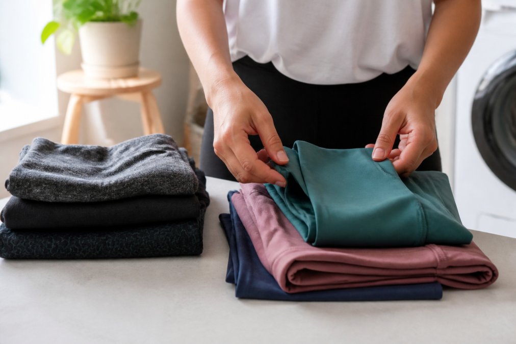 Close-up of hands sorting folded athletic wear by fabric type on a clean laundry surface, with moisture-wicking and synthetic blend garments separated into different piles, bright natural lighting