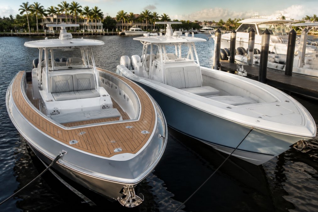 Two high-performance center console fishing boats docked side-by-side at a marina, one with a stepped hull and premium teak accents, the other with a sharper entry and production-grade gelcoat, viewed from a slight elevation to show deck layouts, late afternoon Florida sunlight