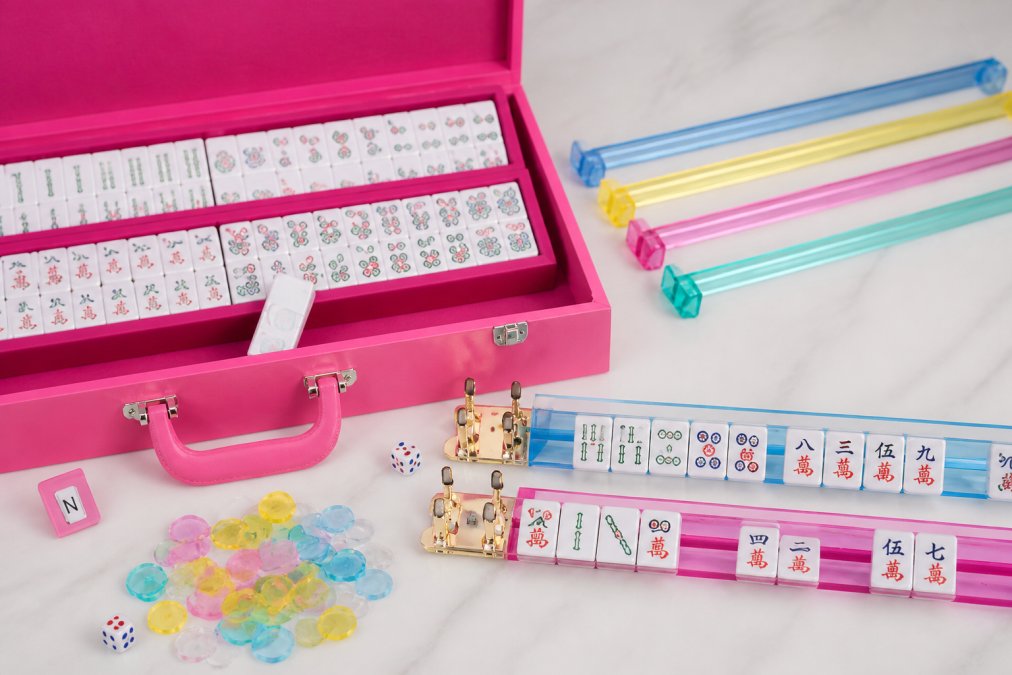 Close-up of colorful mahjong tiles arranged by suit showing bamboo stalks, circular dots, and Chinese characters in natural light, with wind and dragon tiles visible