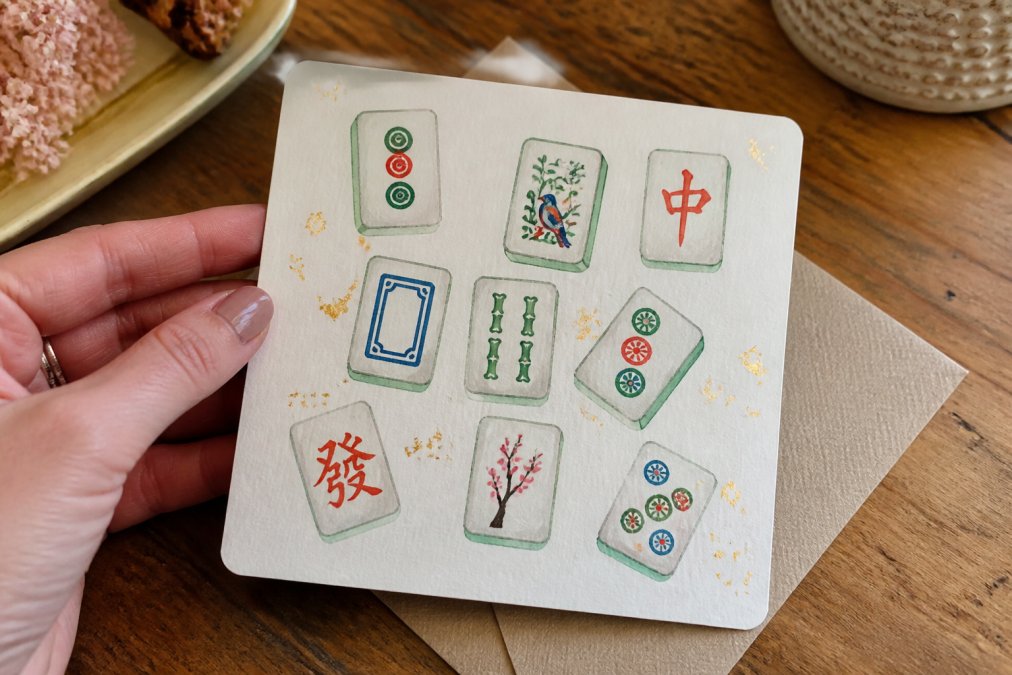 Infographic showing key design elements of a hand-painted mahjong birthday card with gold foil accents.