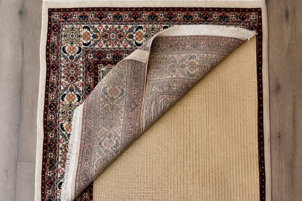 Overhead view of an antique rug with a protective natural rubber pad underneath, showing the underside of the pad and the natural fibers of the hand-knotted rug from above