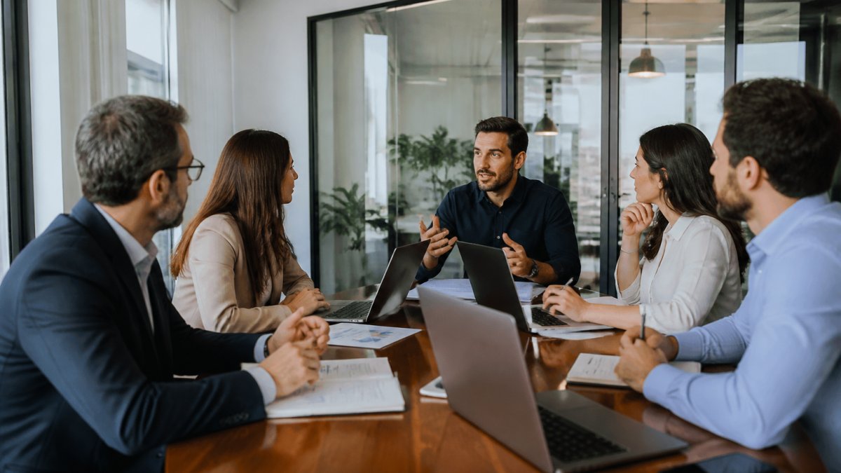 Professional team in modern conference room reviewing cloud migration strategy on large display screen, team members taking notes and discussing plans with laptops open