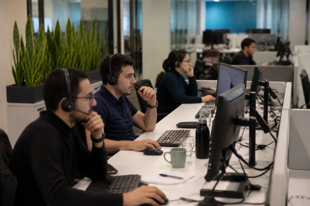 Security operations center team monitoring multiple screens displaying network activity and threat alerts in a modern corporate office, with analysts in headsets focused on real-time dashboards and incident investigation