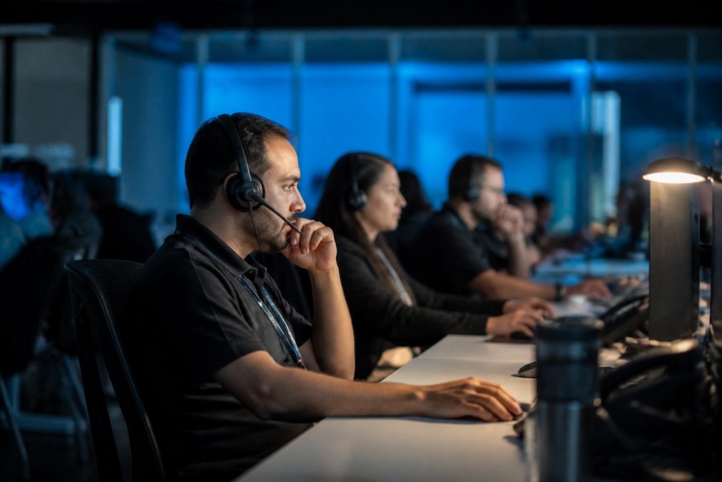 Security operations team monitoring multiple screens displaying real-time network traffic and threat alerts in a modern operations center, with team members analyzing dashboards under soft blue lighting