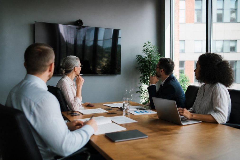 Business team in modern conference room reviewing security infrastructure plans and compliance documents on a large monitor, discussing integration strategy