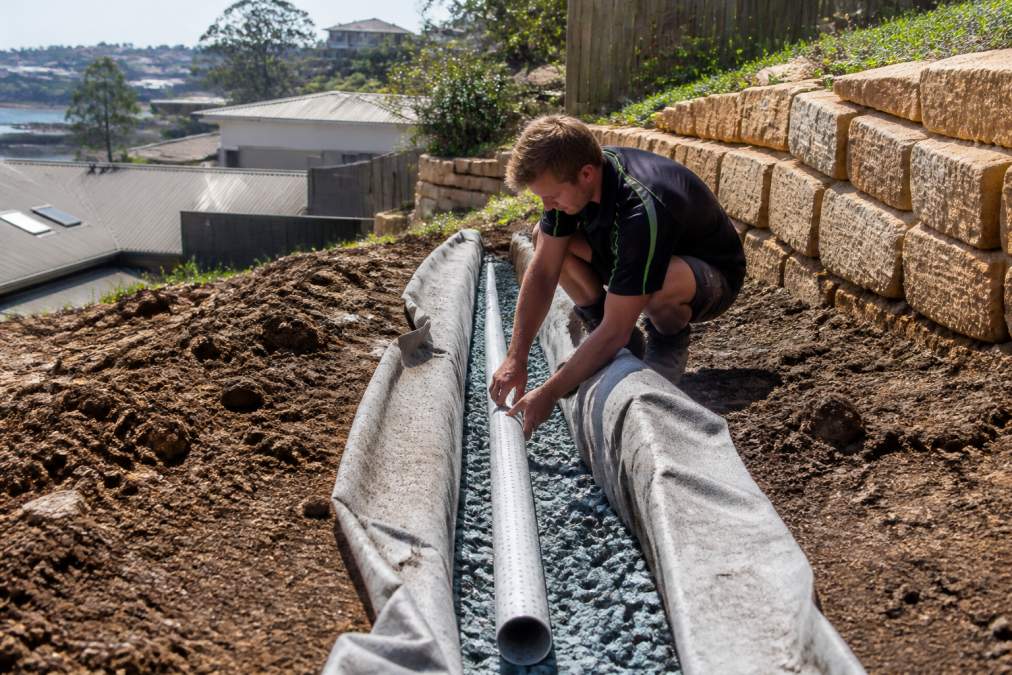 Landscaper installing a French drain with slotted pipes and gravel for managing drainage issues in sloped Sydney gardens
