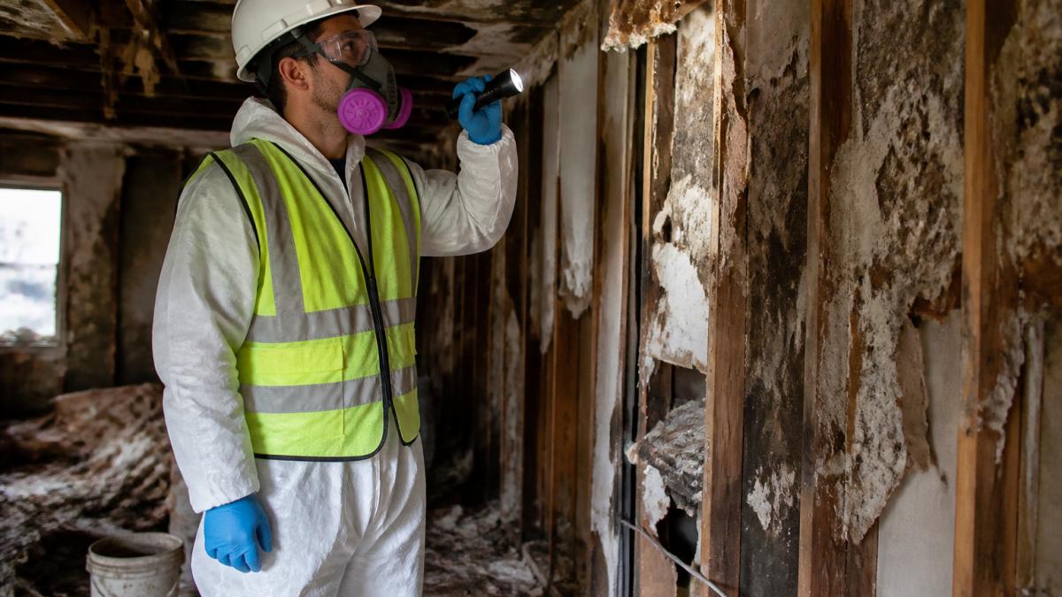 Crew member in full PPE inspecting hazardous debris during foreclosure property debris removal.