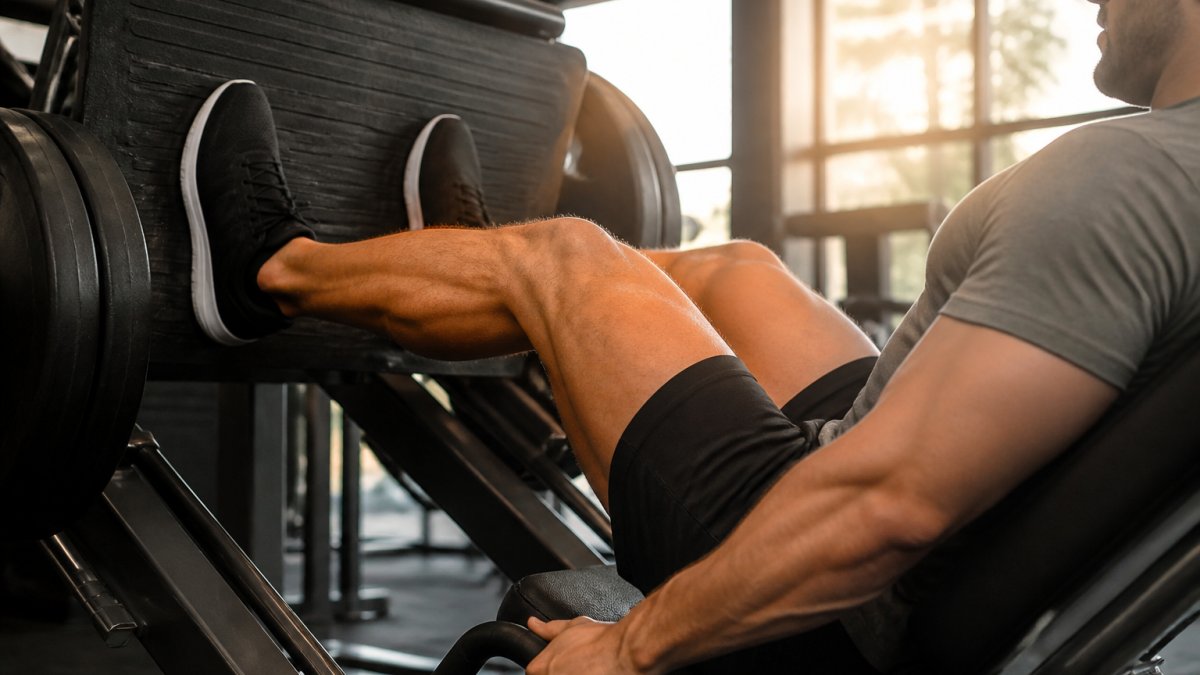 Lifter performing modified leg press with proper knee alignment and controlled range of motion, seated position with natural gym lighting