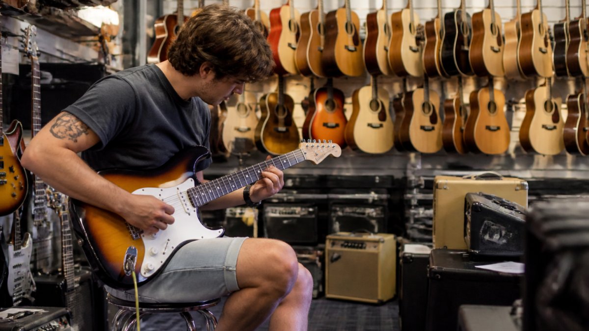 Customer testing an electric guitar inside a well-stocked music shop with acoustic guitars on the walls