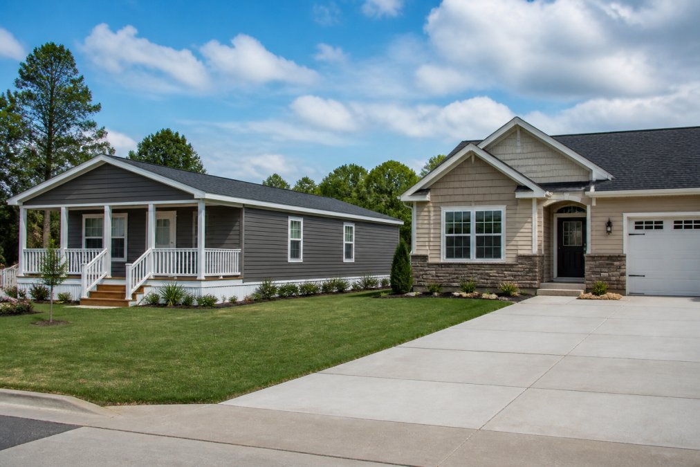 Modern manufactured home exterior positioned next to traditional stick-built home showing contemporary construction quality and finished exterior details in natural daylight