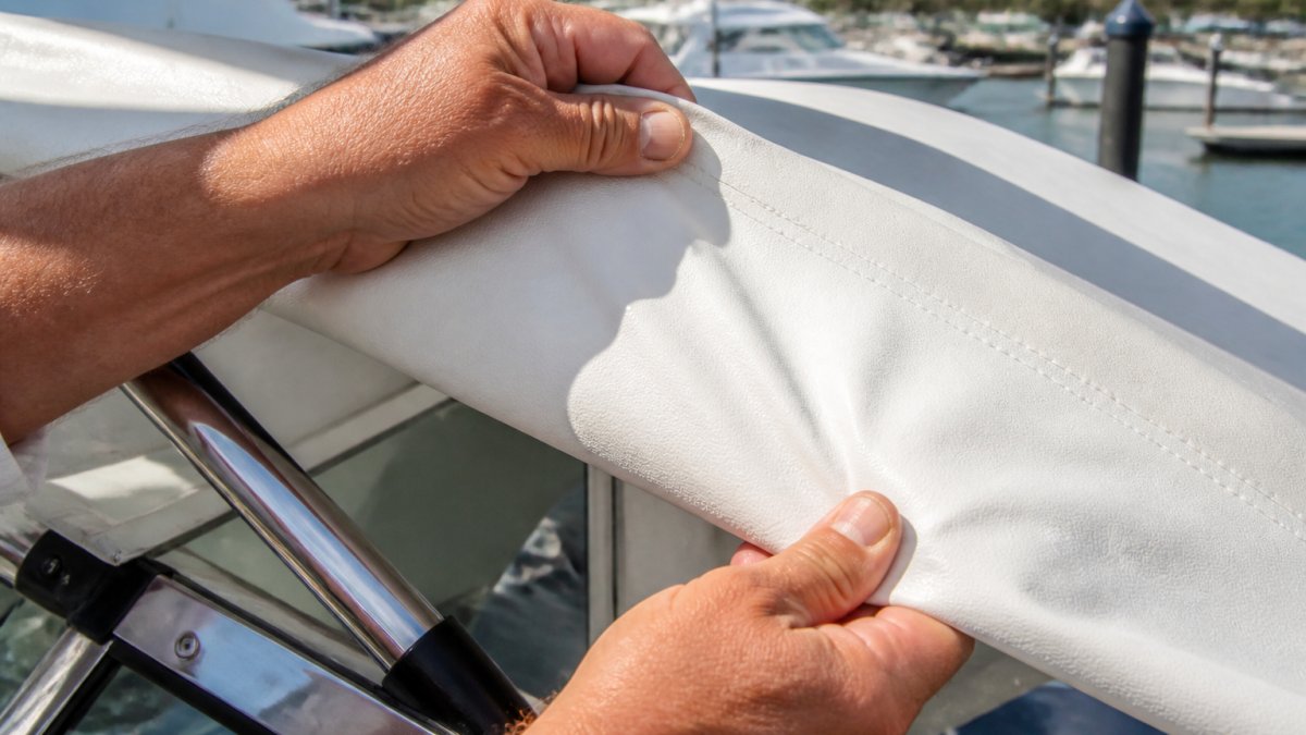 Boat owner testing the flexibility of white marine canvas at a sunny marina to check for fabric brittleness