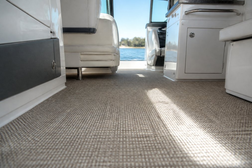 Close-up of textured woven vinyl flooring inside a boat cabin, tight weave pattern visible, sunlight streaming through a window onto the clean surface