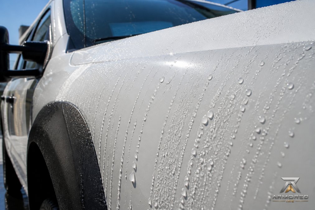 Close-up of work truck's paint surface with ceramic coating applied, showing enhanced gloss and water droplets beading and rolling off the treated surface in bright sunlight