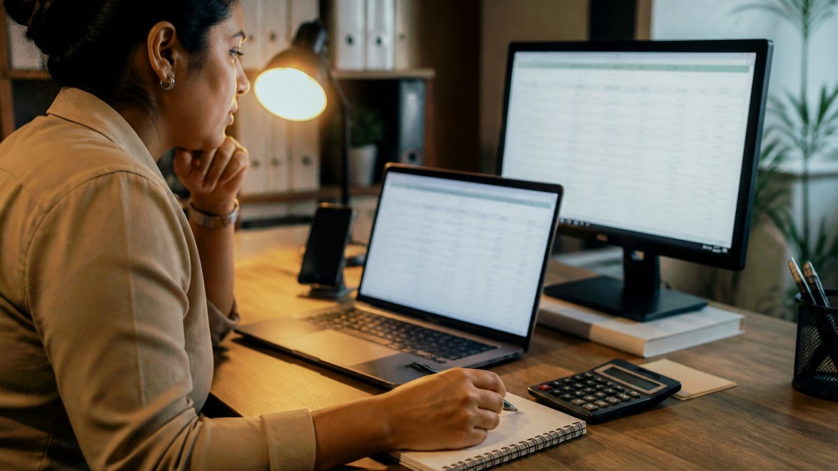 Marketing manager reviewing campaign performance data on a laptop at a desk with a calculator and notepad
