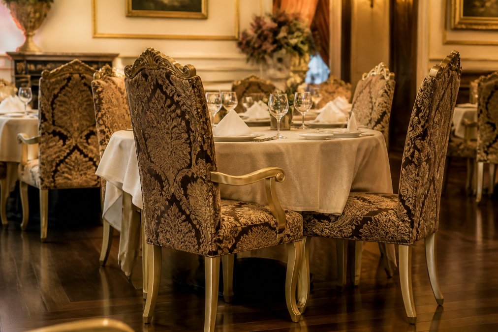 Elegantes Restaurantinterieur mit hochwertigen, gemusterten Polsterstühlen in Barockoptik, die für den täglichen Gastronomiebetrieb ausgelegt sind, in warmem Licht