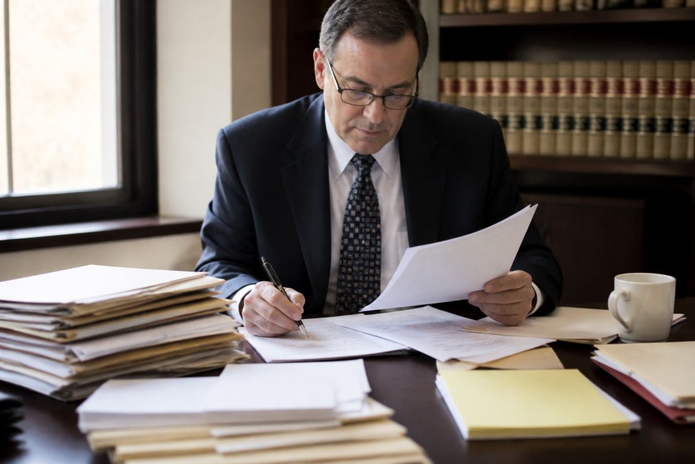 Professional attorney reviewing organized legal documents and financial statements at a desk with careful attention to detail, representing thorough case preparation and billing management